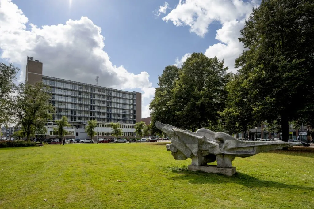 Beeld van een modern kantoorgebouw aan de Jan Tooropstraat met een groot abstract betonnen kunstwerk op een grasveld op de voorgrond.